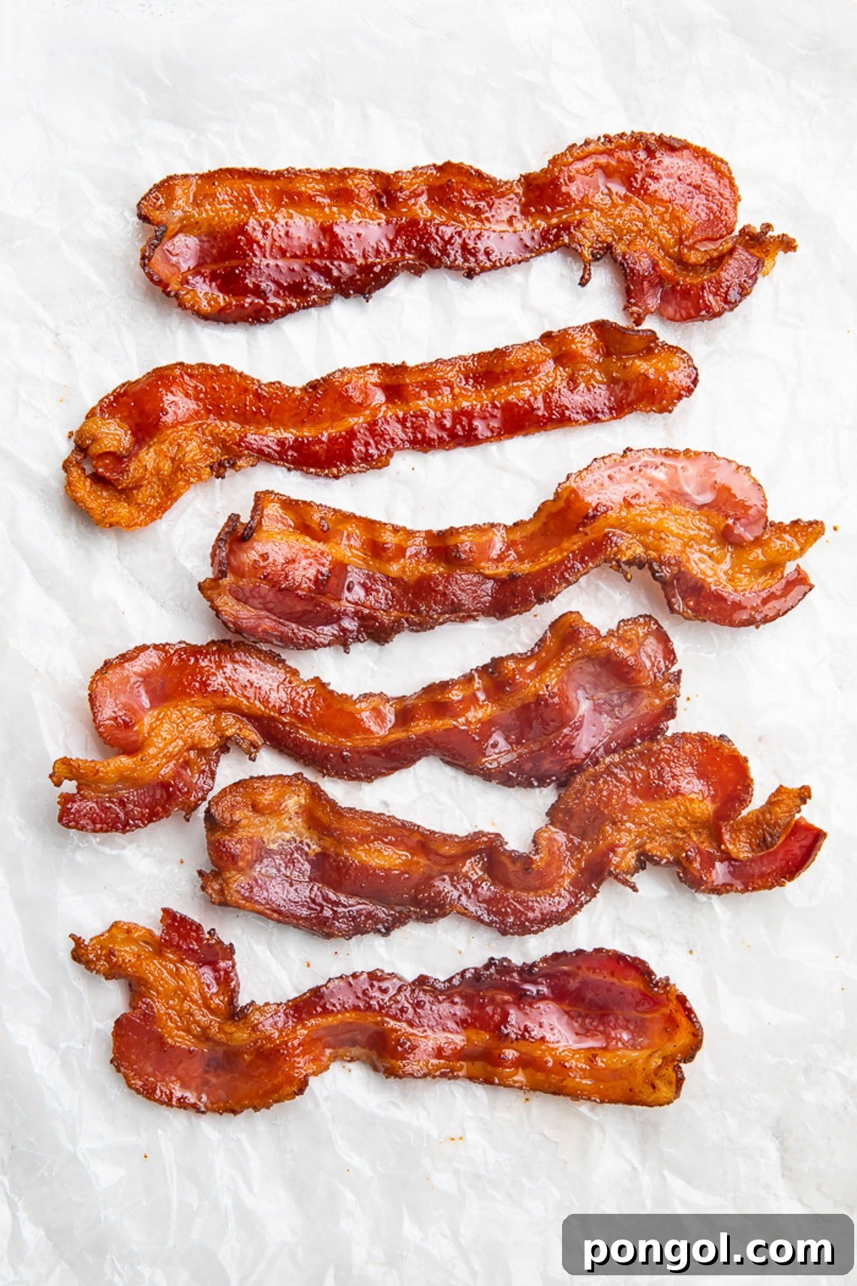 Crispy Air Fryer Bacon 3 Overhead view of crispy strips of air fryer bacon on a sheet of parchment paper, showcasing their golden-brown color and texture.
