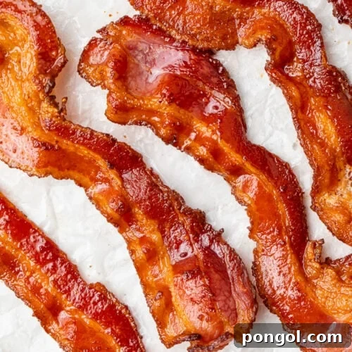 Air fryer bacon strips placed on a sheet of parchment paper, positioned at an angle.