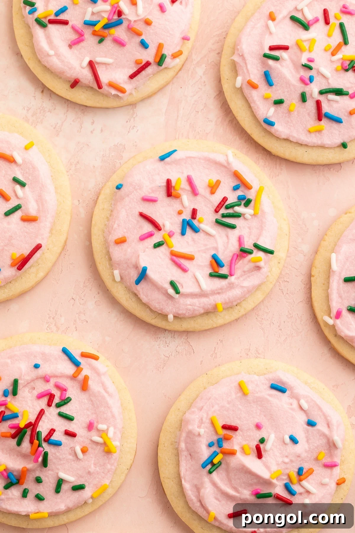Gluten-Free Cut-Out or Drop Sugar Cookies 2 Rows of gluten free sugar cookies topped with pink buttercream frosting and rainbow jimmies on parchment paper.