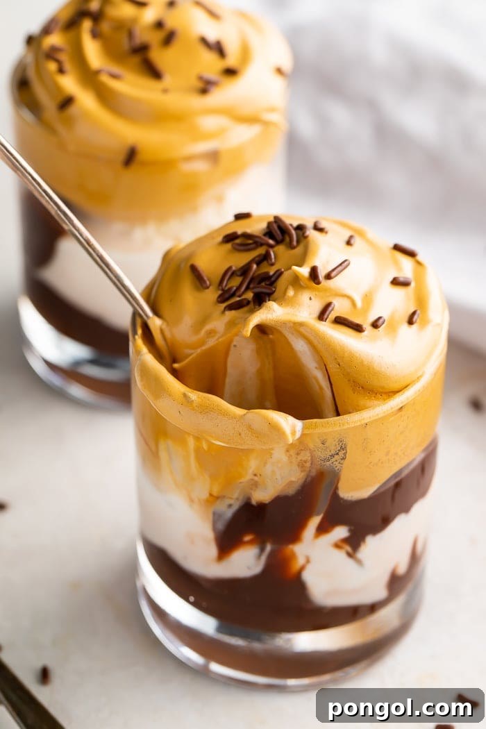Close-up of a whipped coffee ice cream sundae showing layers of fudge, ice cream, and a fluffy whipped coffee topping.