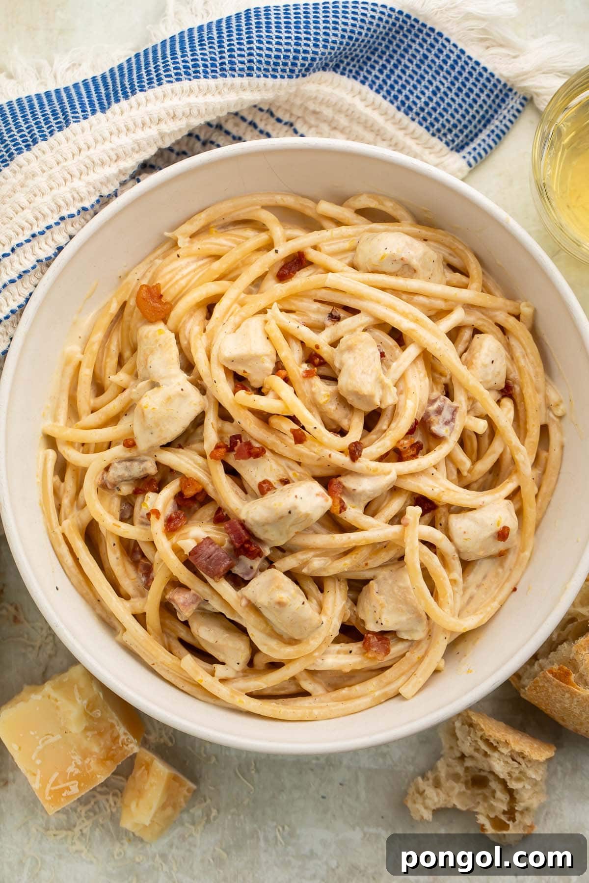 A large white bowl of creamy chicken carbonara on a table with a blue and white kitchen towel, invitingly garnished with fresh herbs and parmesan.