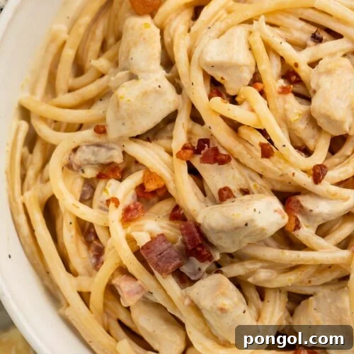 Close-up of a large white bowl of creamy chicken carbonara on a table with a blue and white kitchen towel.