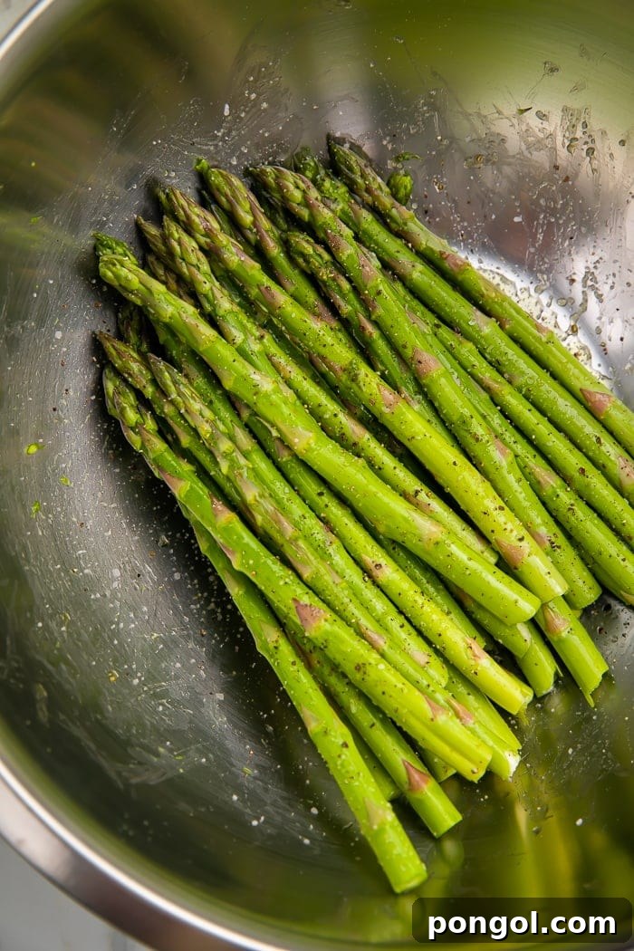 Air fryer asparagus being tossed with olive oil and seasonings