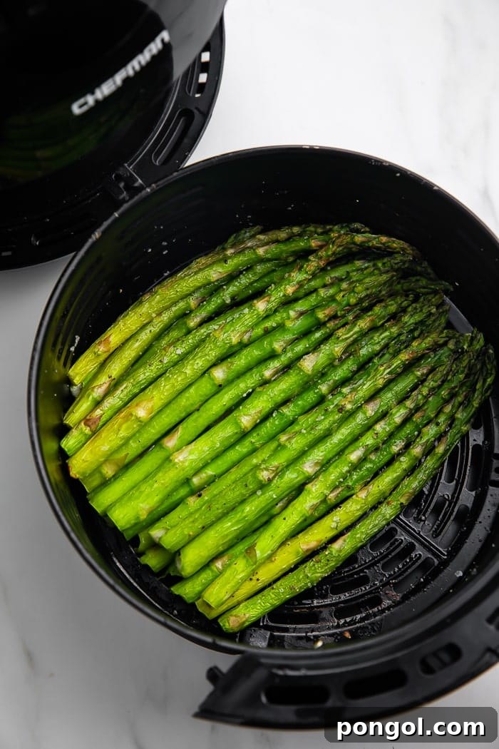 Air fryer basket filled with seasoned asparagus, ready for cooking