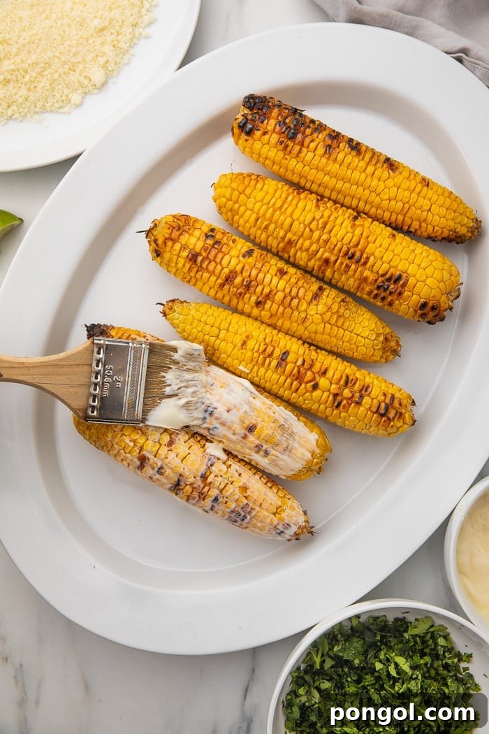 Preparing Elote by spreading mayonnaise on grilled corn