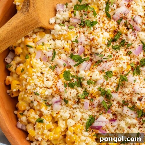 Close-up photo of a large wooden bowl holding a Mexican street corn salad, garnished with cilantro and chili powder.