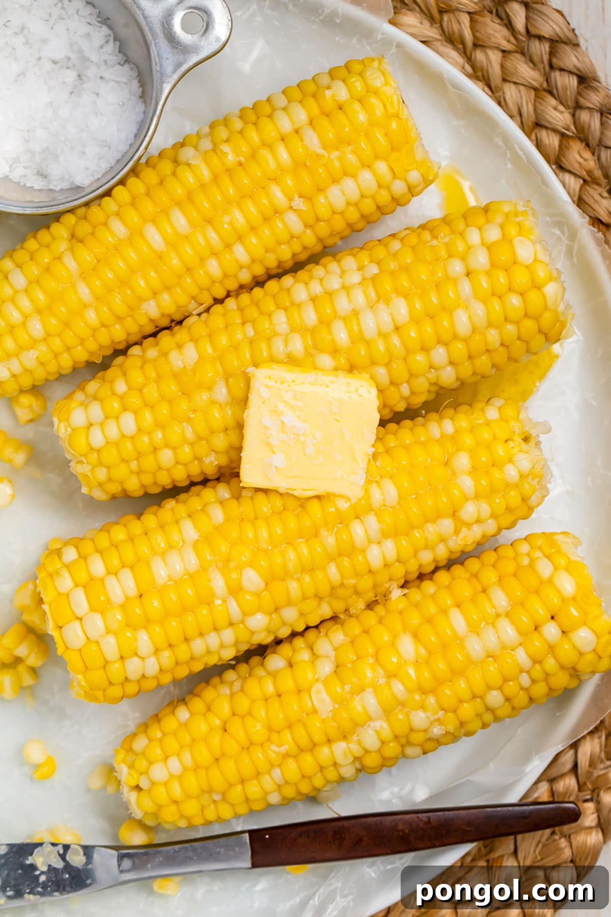 Perfectly Boiled Corn on the Cob 2 4 ears of boiled corn on the cob laying on a white oval platter on a woven placemat.