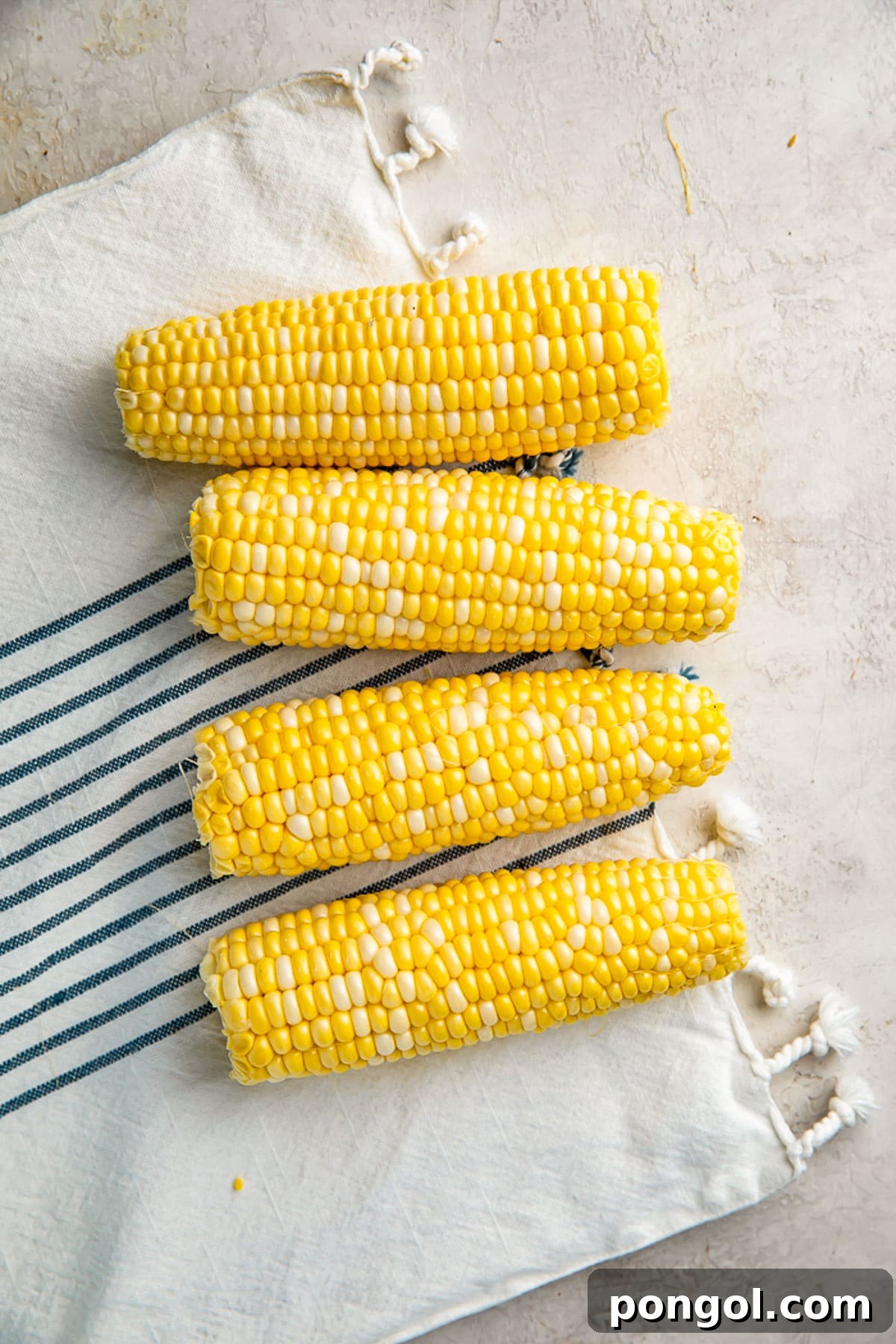 Perfectly Boiled Corn on the Cob 3 4 ears of raw, shucked corn on the cob on a neutral table with a cloth napkin.