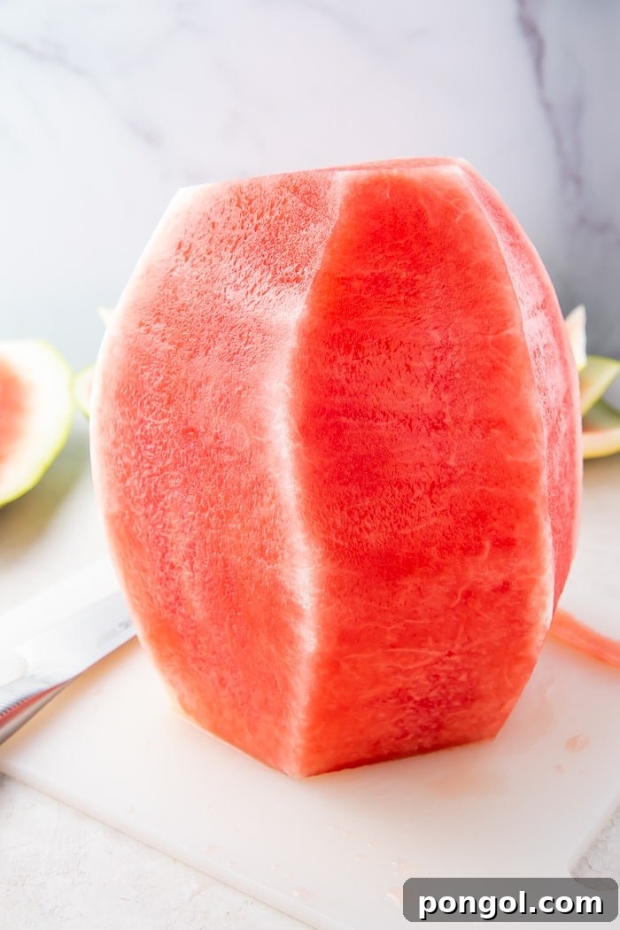 A fully peeled watermelon standing on a cutting board, completely stripped of its green rind, revealing smooth pink flesh.
