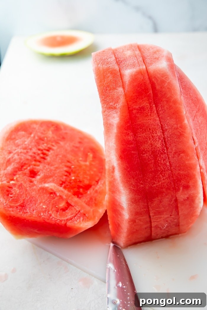 A peeled watermelon neatly sliced lengthwise into several uniform 1-inch thick sheets, lying flat on a cutting board.