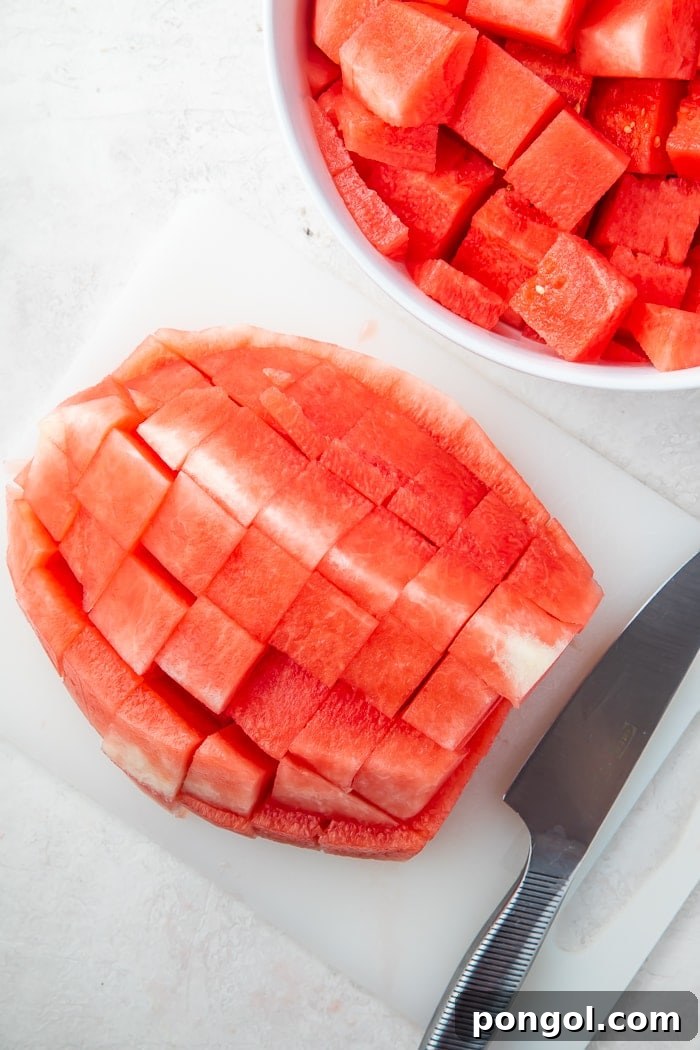 A cutting board showcasing precisely cut 1-inch watermelon cubes, with a portion already transferred to a bowl.