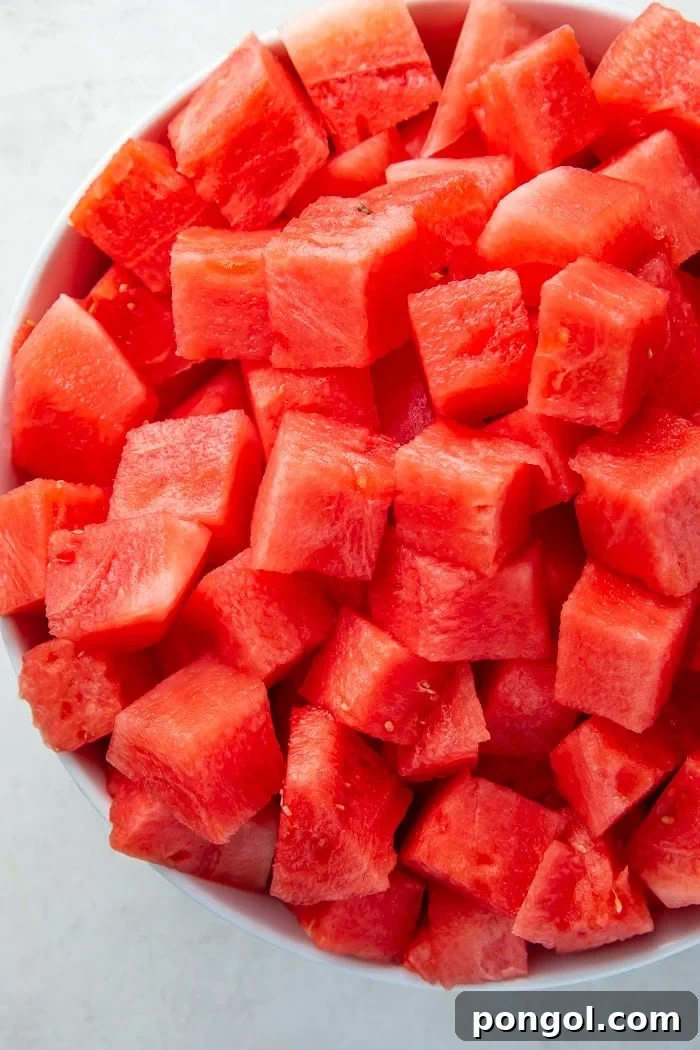 A large, clear glass bowl overflowing with fresh, vibrant watermelon cubes, ready to be served.