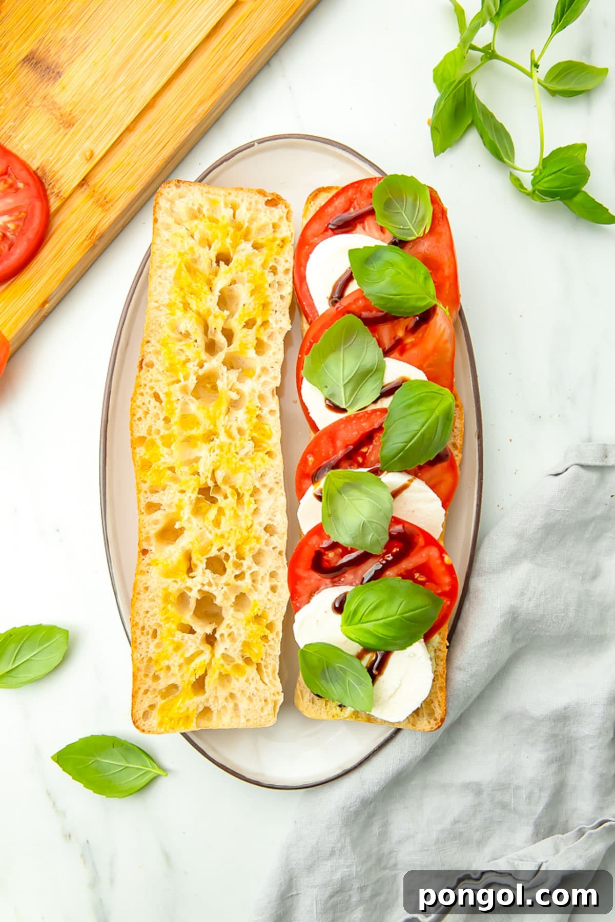 Top-down view of a Caprese sandwich resting on a plate, with the top piece of bread slightly moved to reveal alternating slices of mozzarella and tomato topped with basil and balsamic glaze.