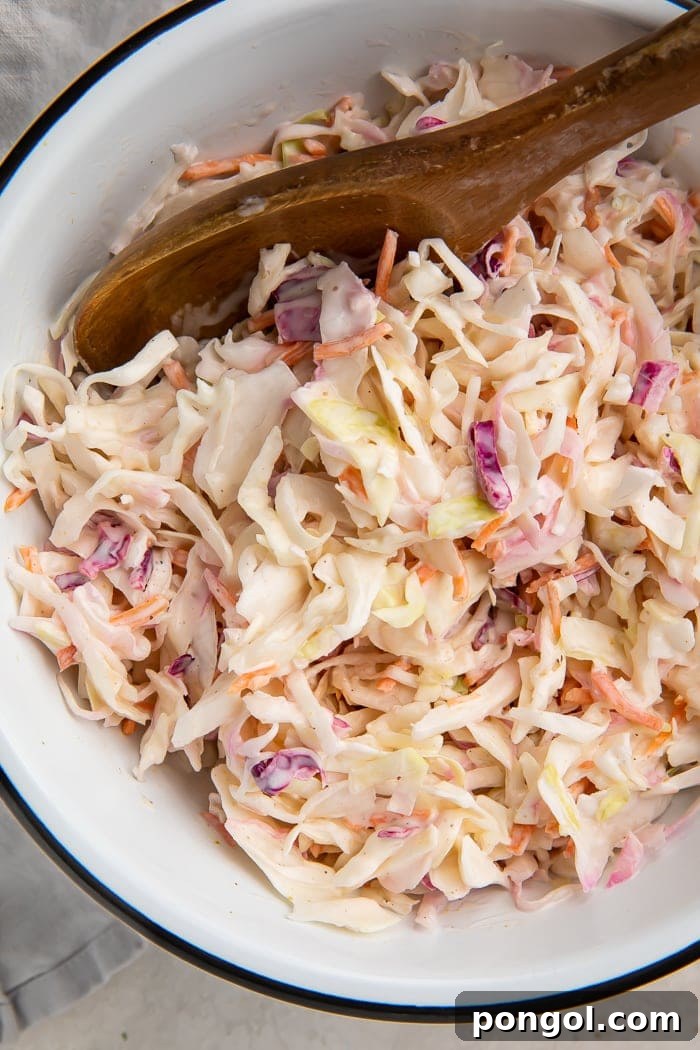 Keto coleslaw in a bowl with a wooden spoon, ready to be served.