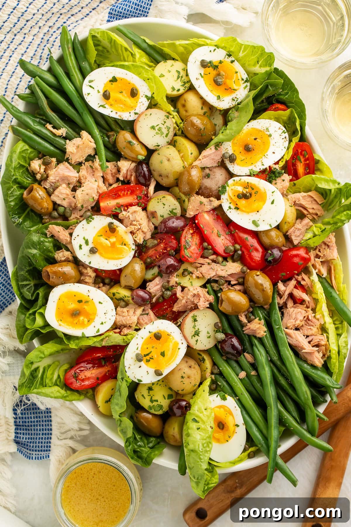 A vibrant Nicoise salad on an oval platter with potatoes, green beans, hard-boiled eggs, crisp lettuce, olives, capers, ripe tomatoes, and flaked tuna.