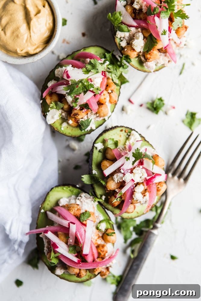 Halved avocados stuffed with a hearty mixture of tuna salad and chickpeas, garnished with herbs.