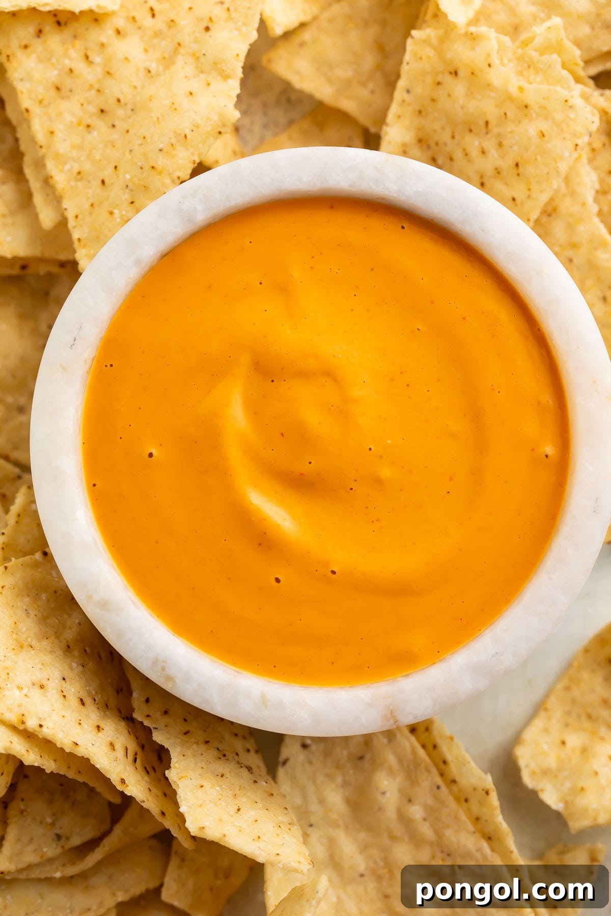 Overhead view of a white bowl of vibrant orange vegan nacho cheese sauce, ready to be enjoyed.