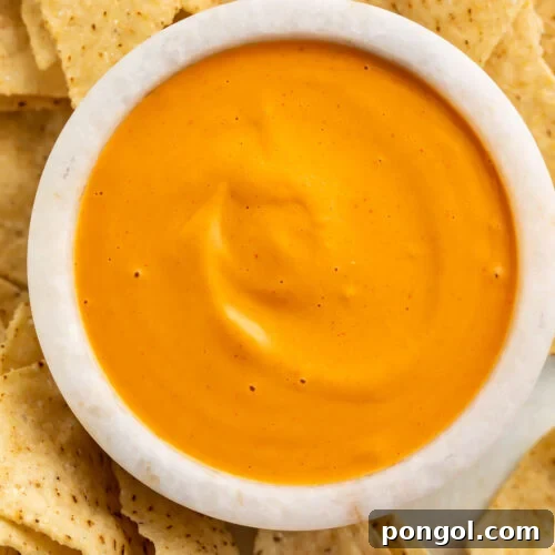 Overhead view of a white bowl of vibrant orange vegan nacho cheese sauce.
