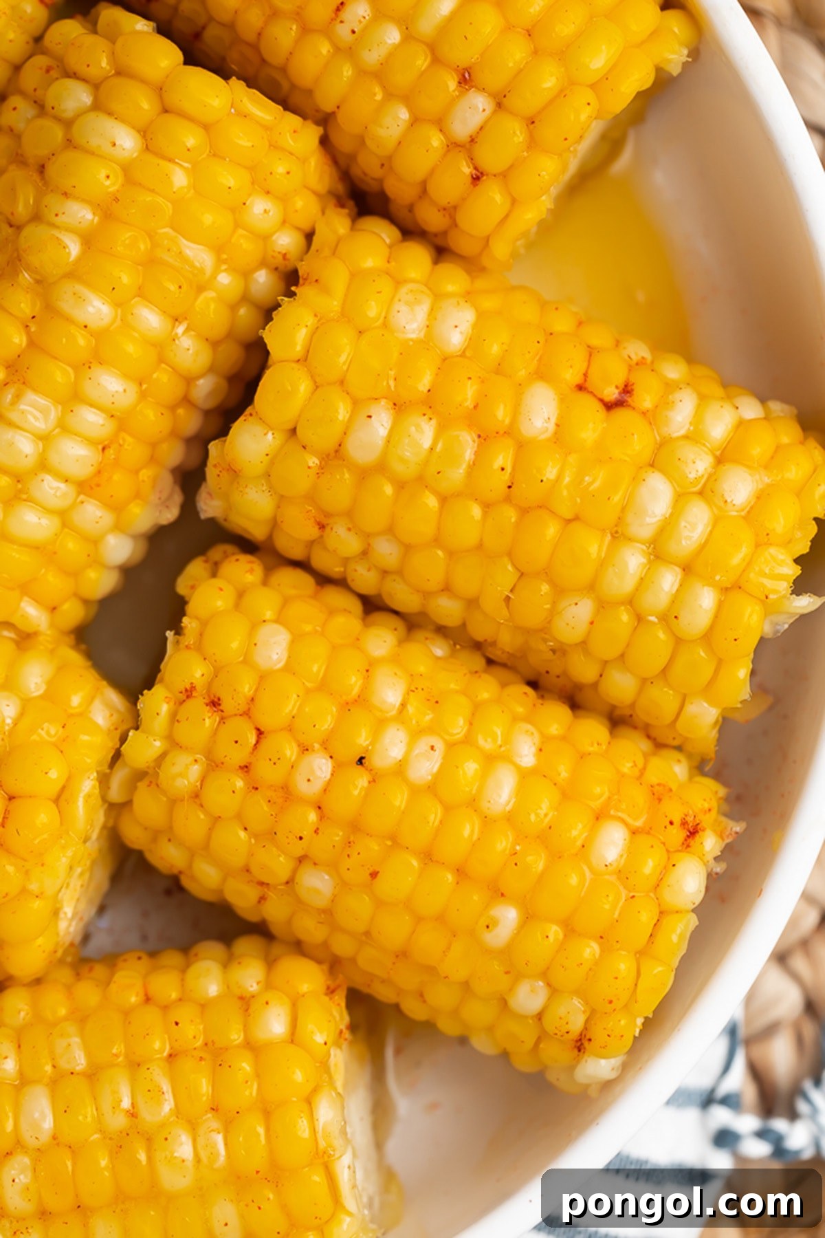 Instant Pot Honey Butter Corn Perfection 3 Instant Pot corn on the cob with a honey butter glaze in a large white bowl on a wicker placemat.