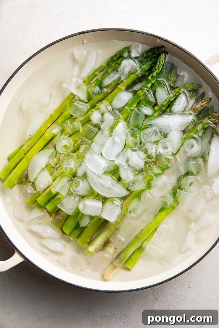 Blanched asparagus chilling in an ice bath in a skillet.
