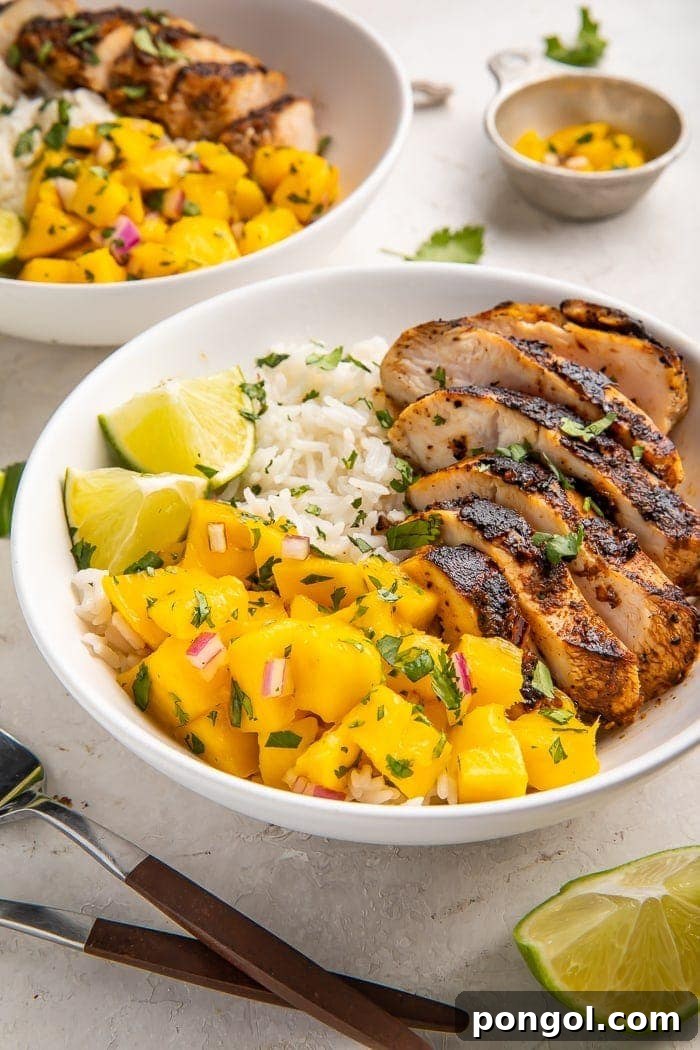 A vibrant bowl of jerk chicken served with creamy coconut rice and fresh, colorful mango salsa, garnished with cilantro.