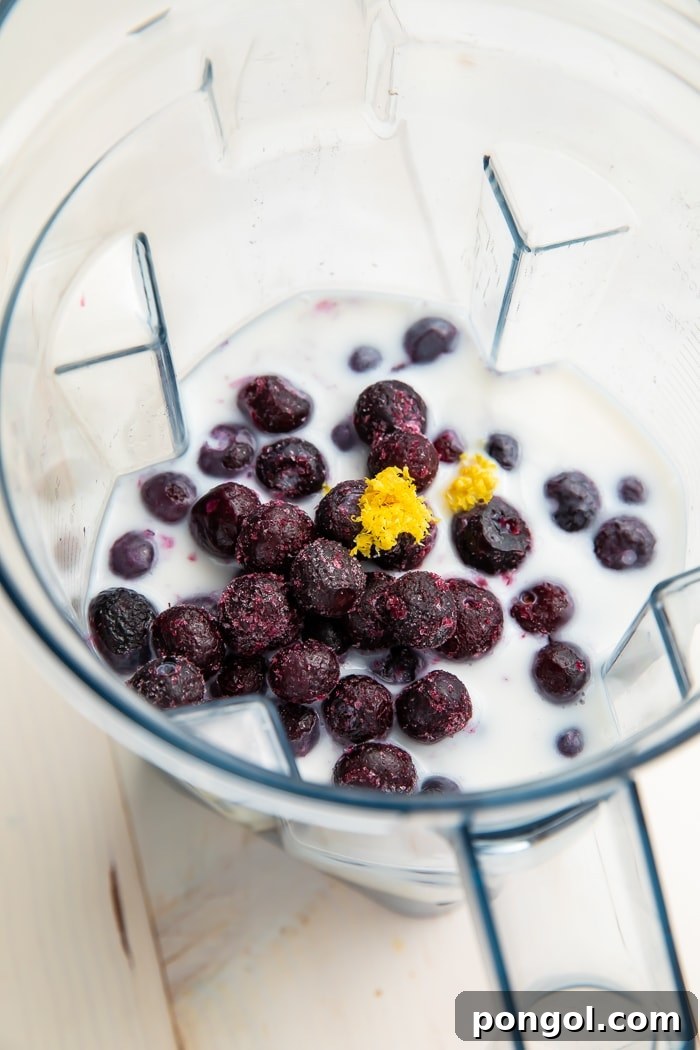 A close-up of a glass of blueberry smoothie, showcasing its vibrant purple color and smooth texture, with fresh blueberries sprinkled on top.