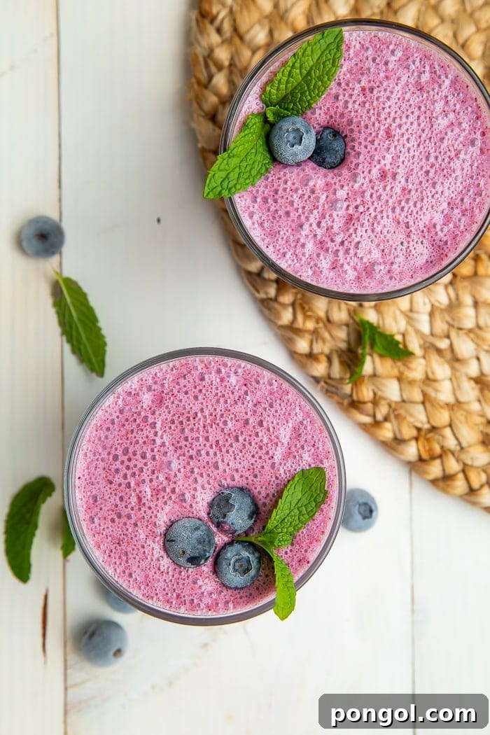 Another perspective of a blueberry smoothie, highlighting the creamy foam and a few whole blueberries visible in the glass, ready to be enjoyed.