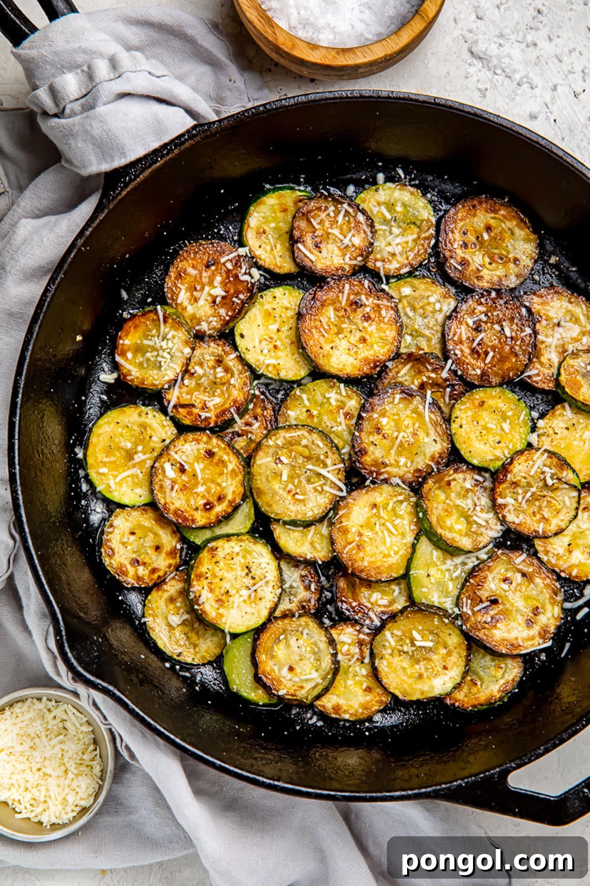 Crispy sauteed zucchini discs topped with finely shredded cheese, ready to be served.