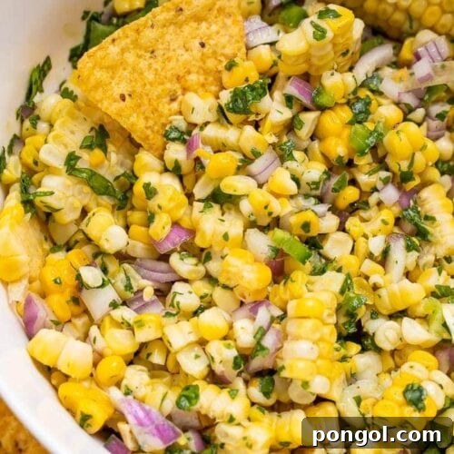 A bowl of fresh corn salsa with a spoon, highlighting the texture and vibrant colors.