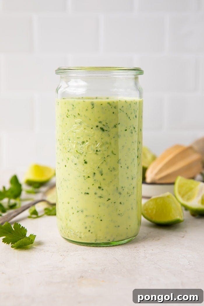 A glass jar filled with luscious, vibrant green cilantro lime dressing, garnished with fresh herbs, ready for use.