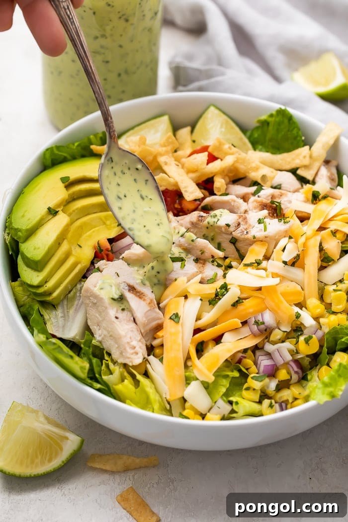 Creamy cilantro lime dressing being generously drizzled over a vibrant, fresh green salad with various toppings.