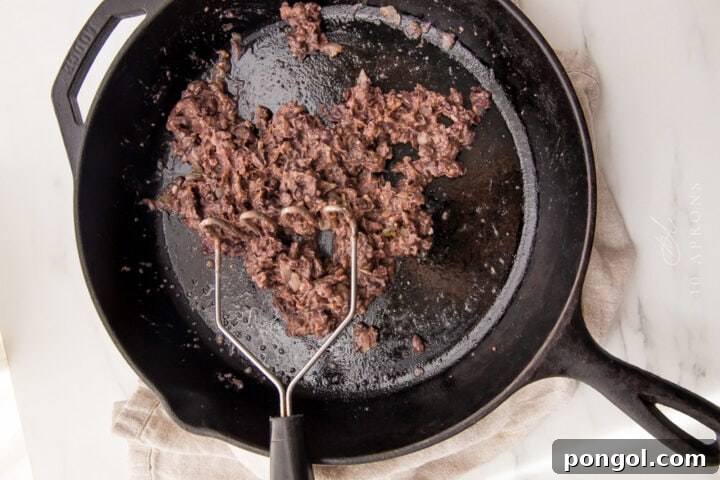 Mashed black beans in a large black cast-iron skillet, showing the initial mash.