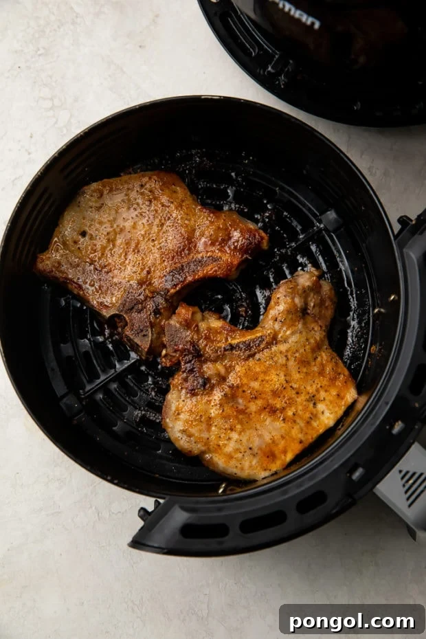 Pork chops cooking to a golden brown in the air fryer basket.