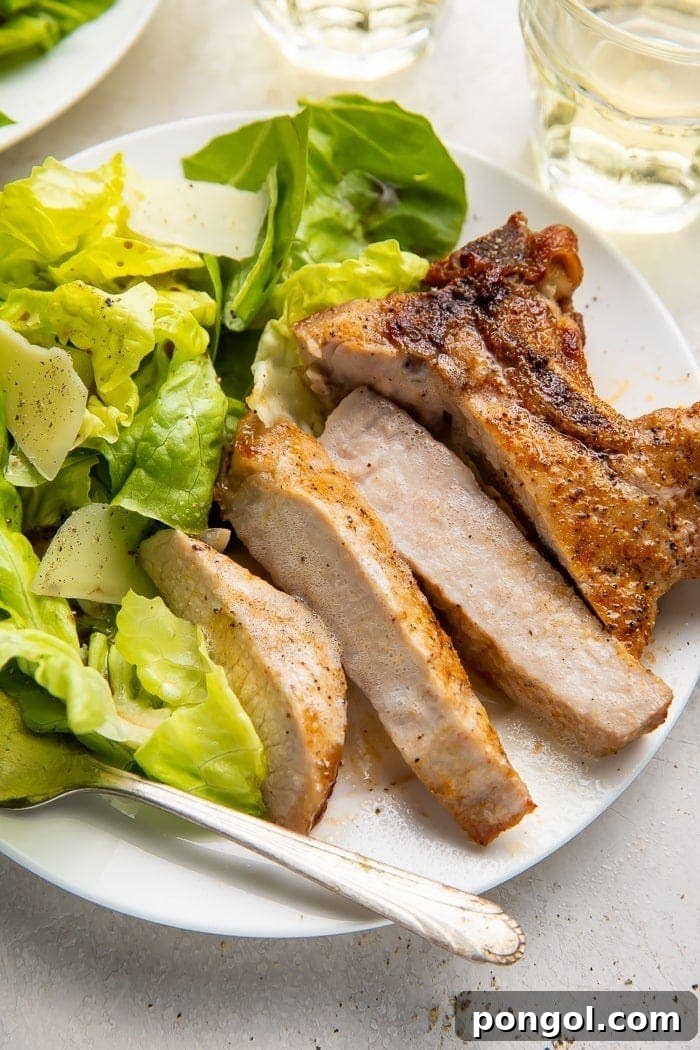 A perfectly sliced and tender air fryer pork chop, revealing its juicy interior, served on a plate next to fresh green lettuce.