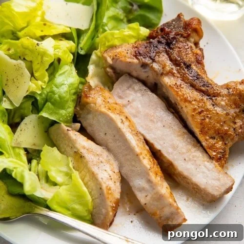 Sliced pork chop cooked in the air fryer with a bed of green veggies on a white plate