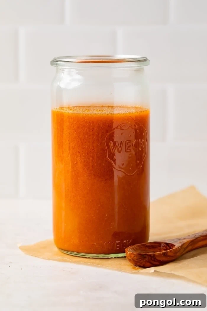 Buffalo sauce in a clear glass jar with a wooden spoon