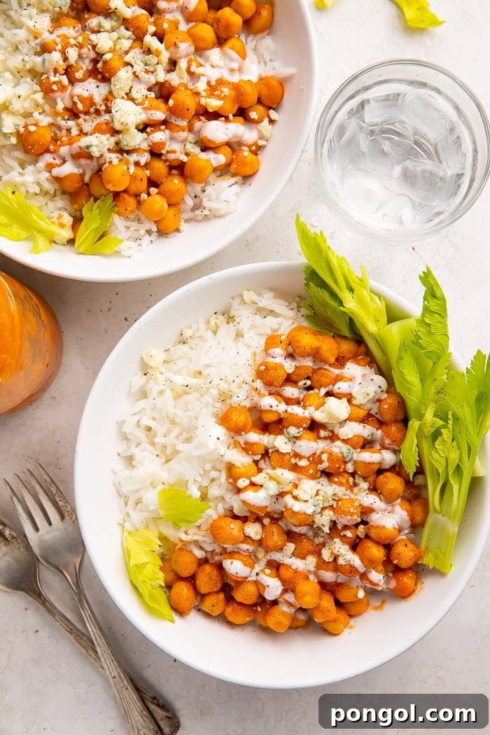 Fired Up Buffalo Chickpea Bowl 4 Two vibrant buffalo chickpea bowls ready to serve, each featuring creamy buffalo-coated chickpeas nestled on white rice, generously topped with ranch dressing, blue cheese crumbles, and fresh celery sticks for garnish.