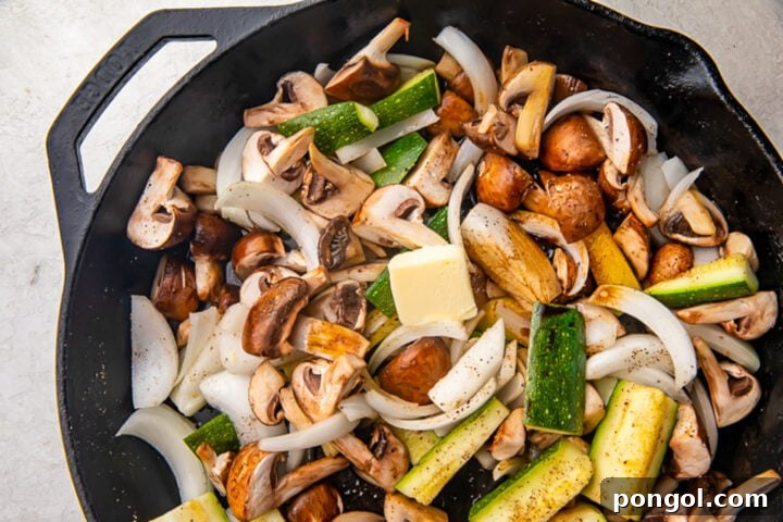 Fresh white onion, baby bella mushrooms, and zucchini sizzling in a large cast-iron skillet on a stove burner.