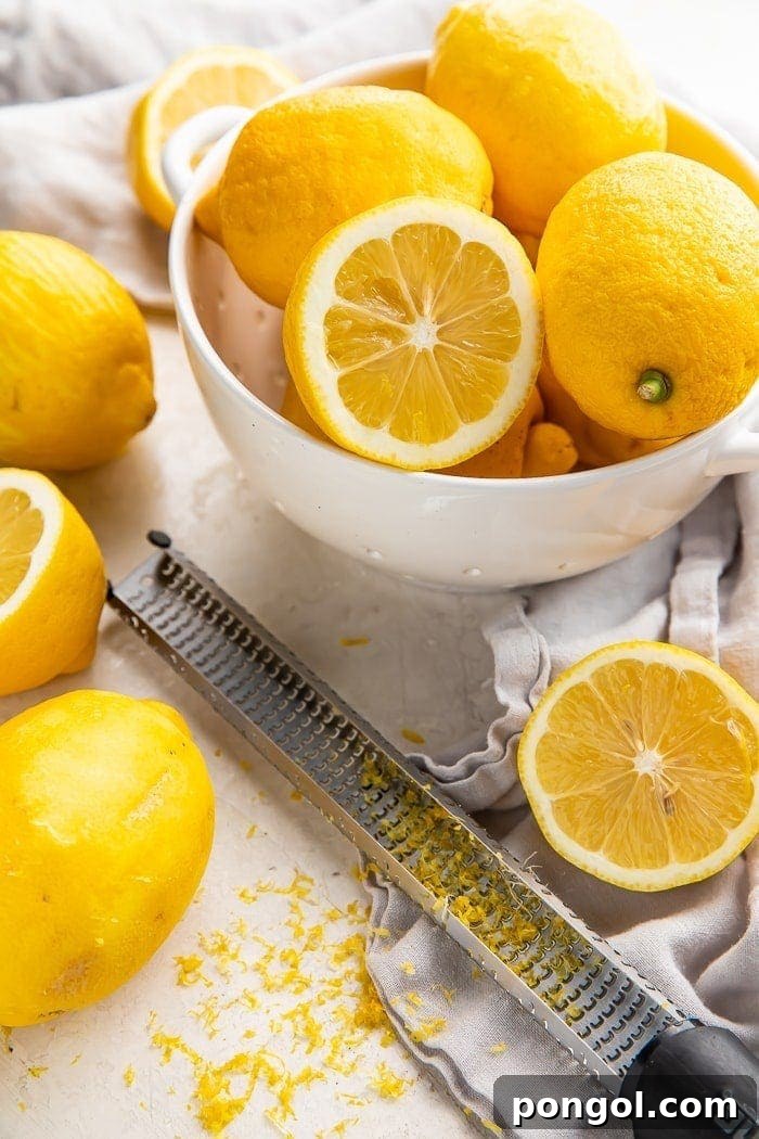 a bowl of lemons surrounded by sliced lemons, a microplane, and lemon zest