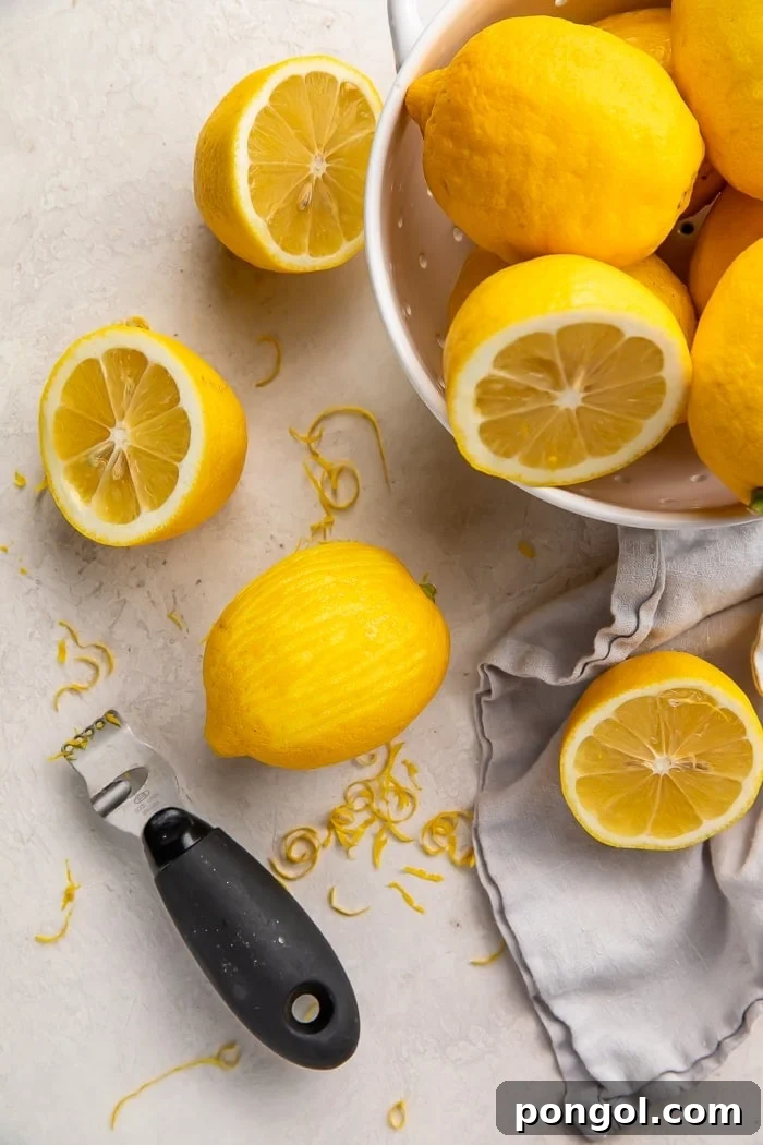 a zested lemon surrounded by lemon zest, a zester, and a colander of lemons