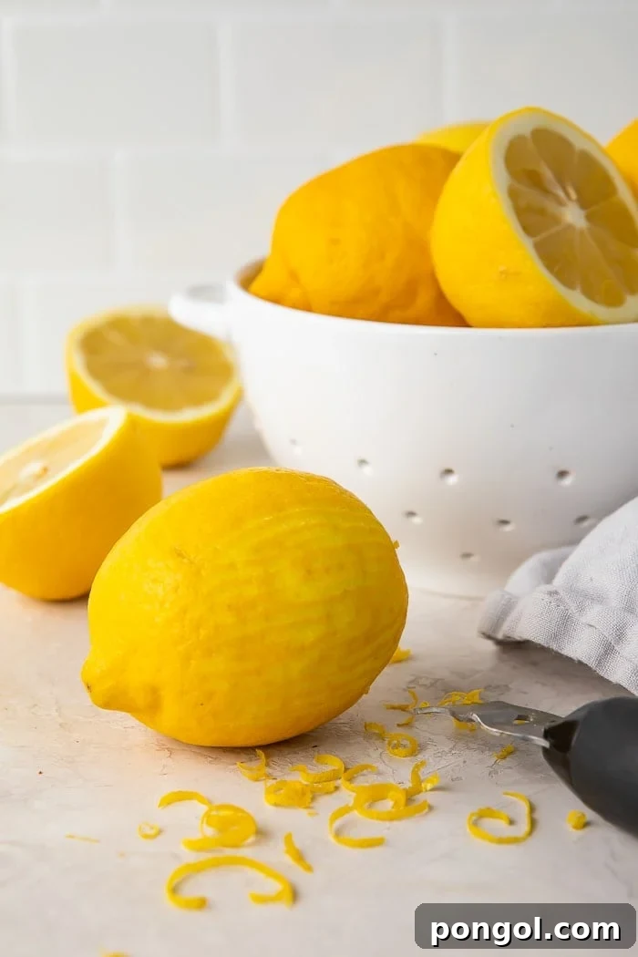 a zested lemon surrounded by lemon zest, a zester, and a colander of lemons