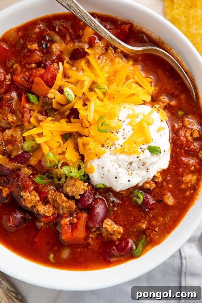 Ultimate Instant Pot Turkey Chili 4 Close-up of turkey chili garnished with shredded cheddar cheese, green onions, and sour cream