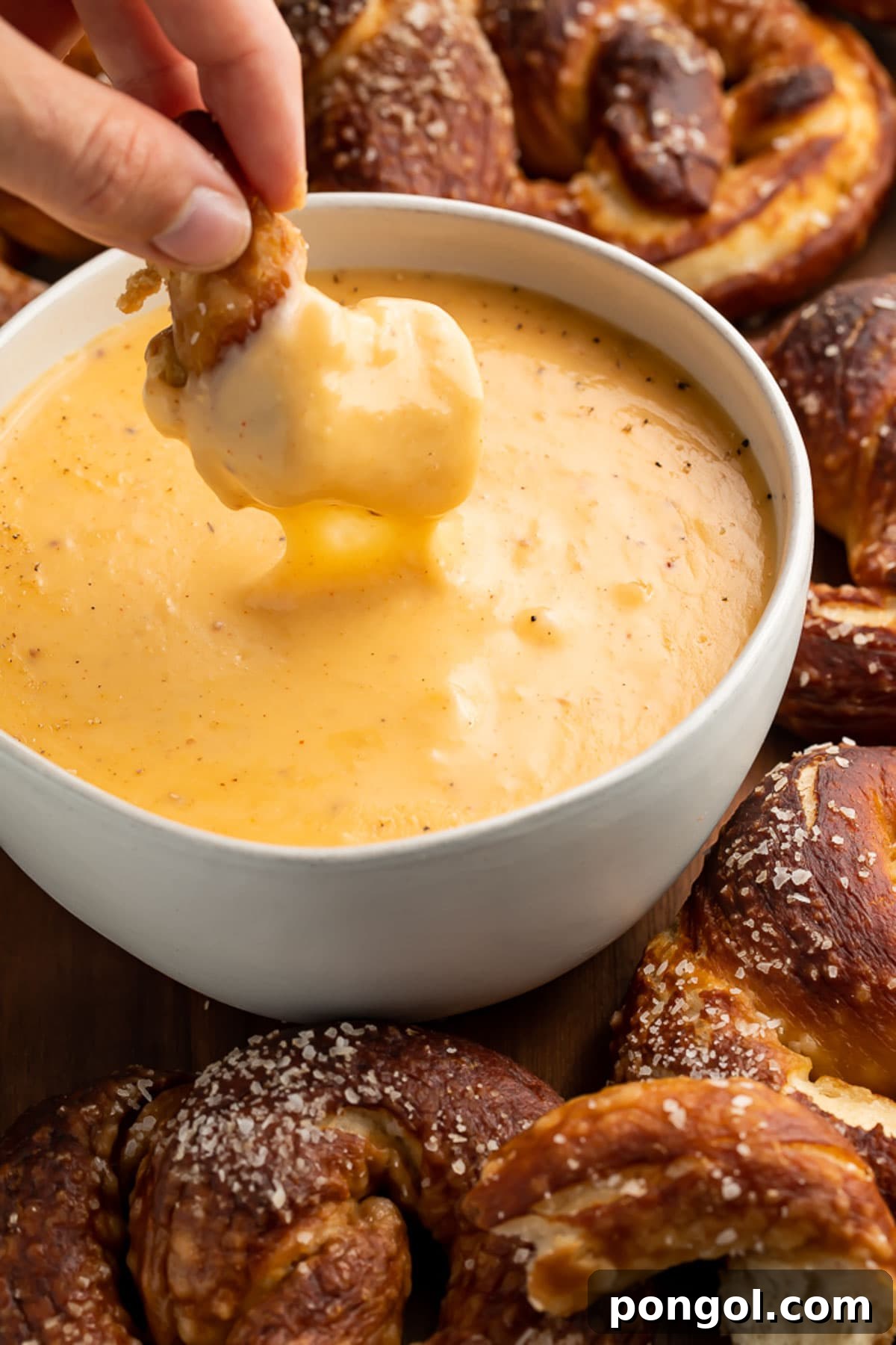 A woman's hand dipping a soft pretzel into a bowl of rich beer cheese dip.