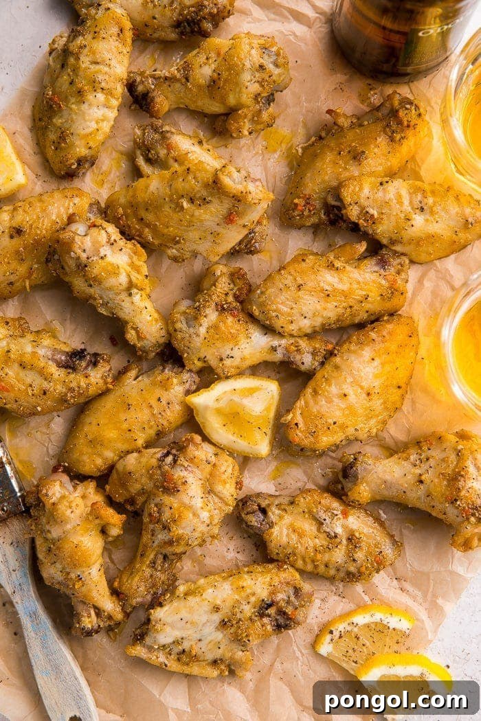 Zesty Lemon Pepper Wings 2 Crispy baked lemon pepper wings garnished with fresh lemon wedges, arranged on parchment paper with a basting brush nearby.