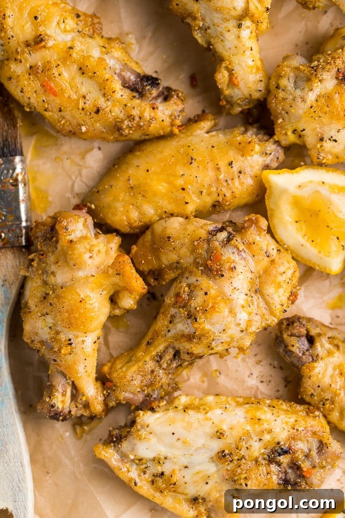 Zesty Lemon Pepper Wings 3 Close-up overhead shot of glistening lemon pepper wings, perfectly baked, with lemon slices and a basting brush on parchment paper, ready to be enjoyed.