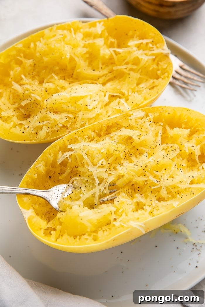 Two halves of cooked spaghetti squash on a white plate with a fork stuck in one half, ready to be shredded into noodles
