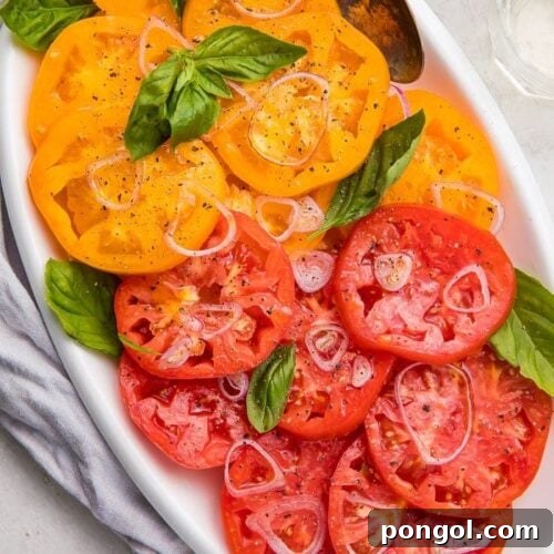 Slices of vibrant red and yellow heirloom tomatoes on a pristine white serving plate, highlighting their natural beauty.