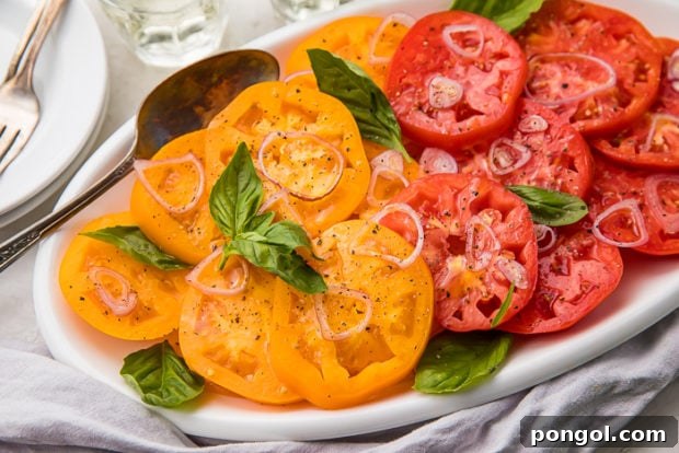 Slices of red and yellow heirloom tomatoes beautifully arranged on a white serving dish, garnished with sliced shallots and fresh basil leaves.