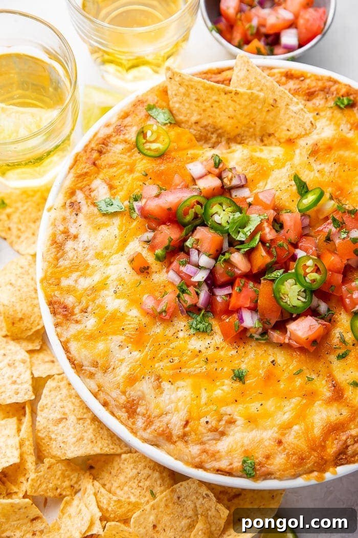 Overhead shot of bean dip in a bowl topped with tomatoes and jalapenos, surrounded by chips and glasses of beer