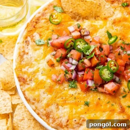 Overhead shot of bean dip in a bowl topped with tomatoes and jalapenos, surrounded by chips and glasses of beer